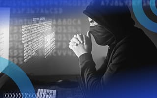 A stereotypical hacker sitting in front of a computer wearing a black hoodie and face mask, hands clasped in front of his face in concentration as he stares at holographic code that’s hovering off the screen.