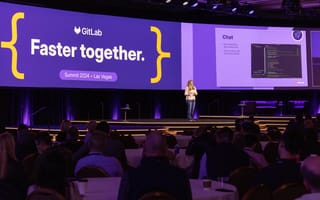 Photo of GitLab leader speaking on a stage with the words " " on screen behind her.