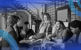 A group of young professionals laughing and exchanging ideas, with the woman in the middle of the group raising her arm triumphantly in the air.