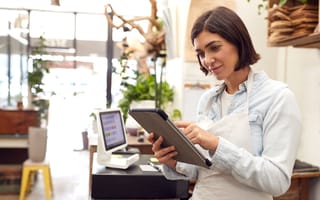 An employee stands in the middle of a store wearing a white apron and holding a tablet device.