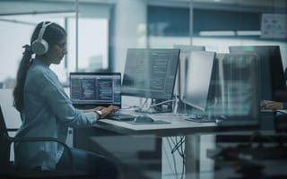 Woman software developer sitting at a desk wearing headphones.