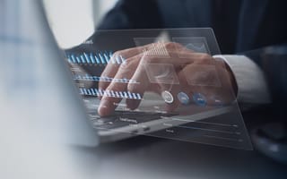 A digital illustration of bag graphs hovers over a hand typing on a laptop keyboard.