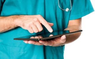 A person wearing scrubs holds a tablet with one hand and hovers their over hand over the device's screen.
