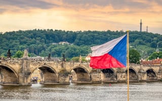 A view of Prague at sunset with Old Town bridge in the background and the Czech flag in the foreground.