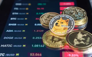 Several gold coins, including one with the dogecoin mascot, lay on top of an electronic screen displaying a list of altcoins on a cryptocurrency exchange.