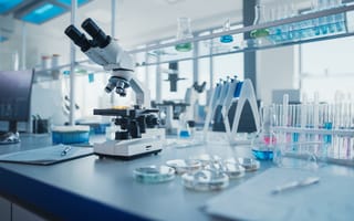 A desk is covered in test tubes, petri dishes, a microscope and other lab tools.