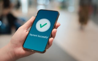 A close up of a hand holding a mobile phone with a green check mark on the screen and text stating "Payment Successful."