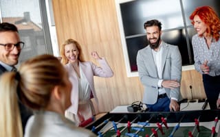 An image of employees laughing while playing a game of foosball together in an office