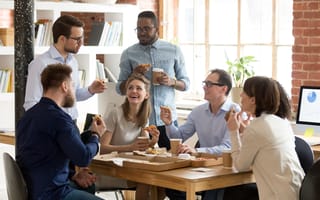 A group of coworkers talk while eating lunch around a table.