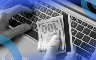 A hand holds a $100 bill and a credit card above a laptop keyboard