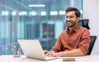 A man sits at a desk typing on a laptop computer.