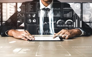 A person in a suit and tie sits at a desk with a digital illustration of various charts and graphs overlaying them to depict business intelligence.