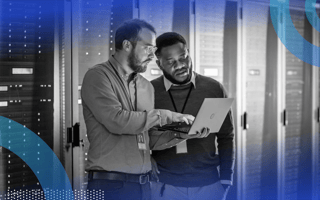 Two database managers reviewing information on a laptop in a server room