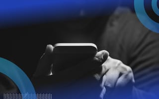 A hacker holds a phone while wearing a hoodie in the shadows.