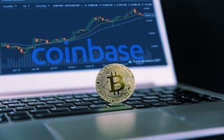 A laptop featuring the word coinbase on the monitor and a coin representing bitcoin on the keyboard.