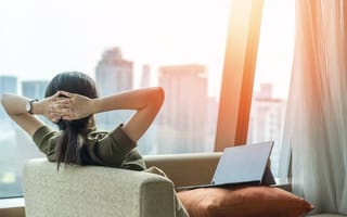 A professional woman leans back in a chair with her hands behind her head while taking a break in an office