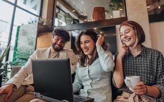 Three team members in an office laugh together while chatting with their coworker virtually