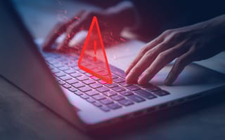 Hands typing on a laptop keyboard with a glowing red warning triangle and exclamation mark overlay.
