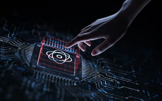 A hand lightly touches a glowing red rectangle with an atomic symbol on a dark, futuristic circuit board.