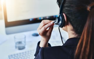 A sales professional wearing a headset sits at a desk in front of a computer monitor.