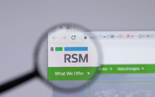 Magnifying glass focuses on the RSM logo on a website's top-left corner, with a green menu bar below labeled "What We Offer" on a computer screen.