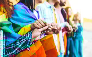 People holding hands while wrapped in a rainbow flag, symbolizing solidarity with LGBTQIA