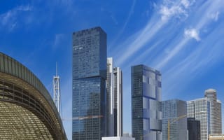 Modern cityscape with tall, sleek glass skyscrapers under a vibrant blue sky.