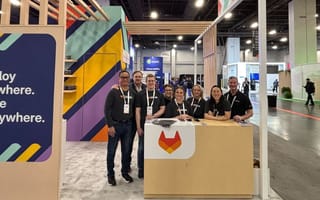 Eight GitLab teammates in GitLab t-shirts stand beneath a ‘GitLab’ sign