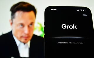 A smartphone screen displays the Grok AI interface with the tagline “Understand the universe,” while a blurred image of Elon Musk appears in the background.