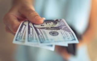 A close up of a hand holding out three $100 bills.