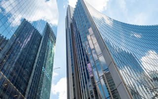 Windows on London high rises reflect the city landscape against the backdrop of a blue sky and clouds.