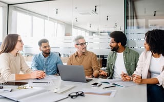 Five team members discuss strategies for a tech initiative while working together at a table in an office