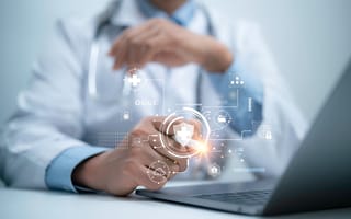 A doctor sits at a desk wearing a white coat and stethoscope with a digital illustration featuring featuring a shield in the image foreground to represent healthtech and patient advocacy.
