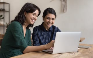 Two smiling women work on a project together in an office