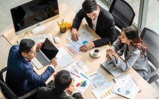 Four office workers sit around a conference table covered in documents.