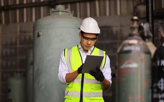 A construction worker in a safety vest and hard hat examines a tablet in an industrial setting, conveying focus and concentration.