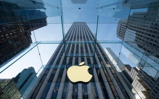 Looking up through a glass ceiling, a large gold Apple logo is centered, surrounded by tall skyscrapers against a blue sky, creating a modern, sleek vibe.