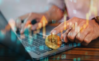 A hand holds a bitcoin over a laptop keyboard, symbolizing cryptocurrency and digital finance.