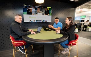 Three smiling DraftKings team members discuss an ongoing project at a table in the company’s office