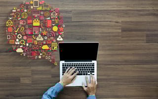 A pair of hands type on a laptop with several icons floating above it in the shape of a conversation bubble.