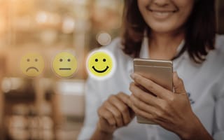 A smiling person uses a smartphone, with three emoticons floating nearby: a sad face, neutral face, and a highlighted happy face, suggesting positive feedback.