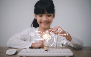 Smiling girl touching a glowing light bulb above a keyboard, symbolizing e-learning.