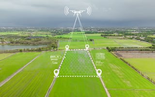 A drone hovers above lush green fields under a cloudy sky, scanning a designated area marked with digital overlays for data collection and mapping.