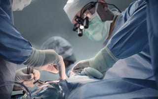Surgeons in blue scrubs and masks perform a precise operation.