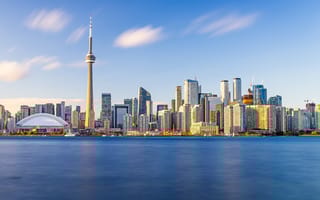 Toronto skyline at dusk with CN Tower and modern skyscrapers reflecting in calm water, under a vibrant blue sky with scattered clouds.