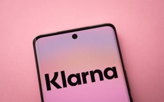 A smartphone screen displaying the Klarna logo on a pink gradient background. The phone is angled slightly against a matching pink surface.