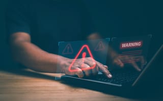 A pair of hands type on a laptop keyboard overlaid by an illustration featuring a red triangle with an exclamation mark in the center and the word WARNING to represent fraud detection.