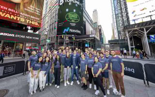 The Topline Pro team poses for a group photo while wearing company-branded T-shirts in front of the Nasdaq building in NYC’s Time Square