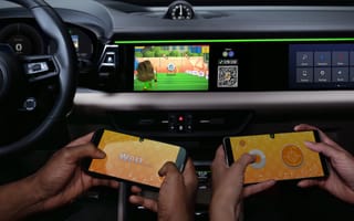 People hold smartphones in a car in front of an infotainment screen.
