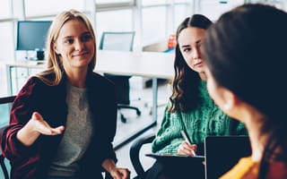 Three sales team members discuss a new strategy while working together in an office